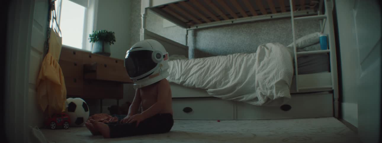 A young child sits on the floor with an astronaut helmet on their head