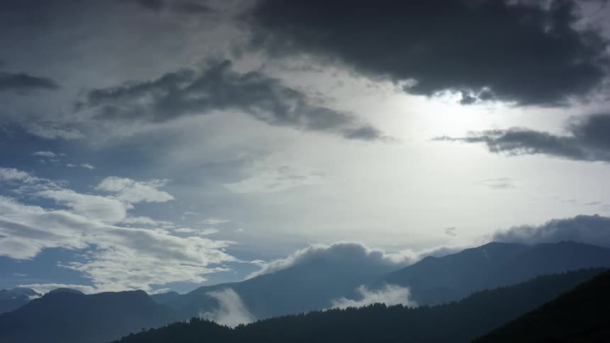 Dark clouds move over mountains with white clouds in the distance