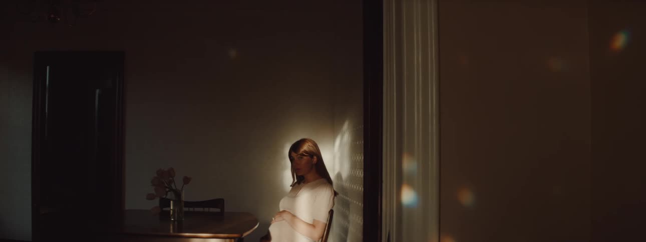 A woman in a room sitting on a chair at a table with a wall and door in the background