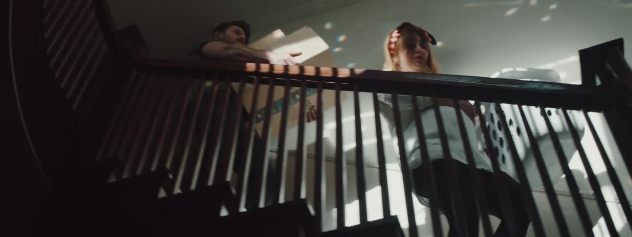A woman carrying a laundry basket down a staircase as a man behind her carries a box
