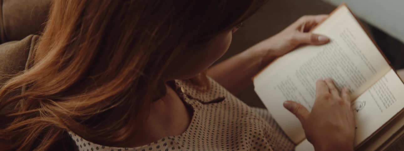 A woman in a room sitting on a couch reading a book and flipping pages