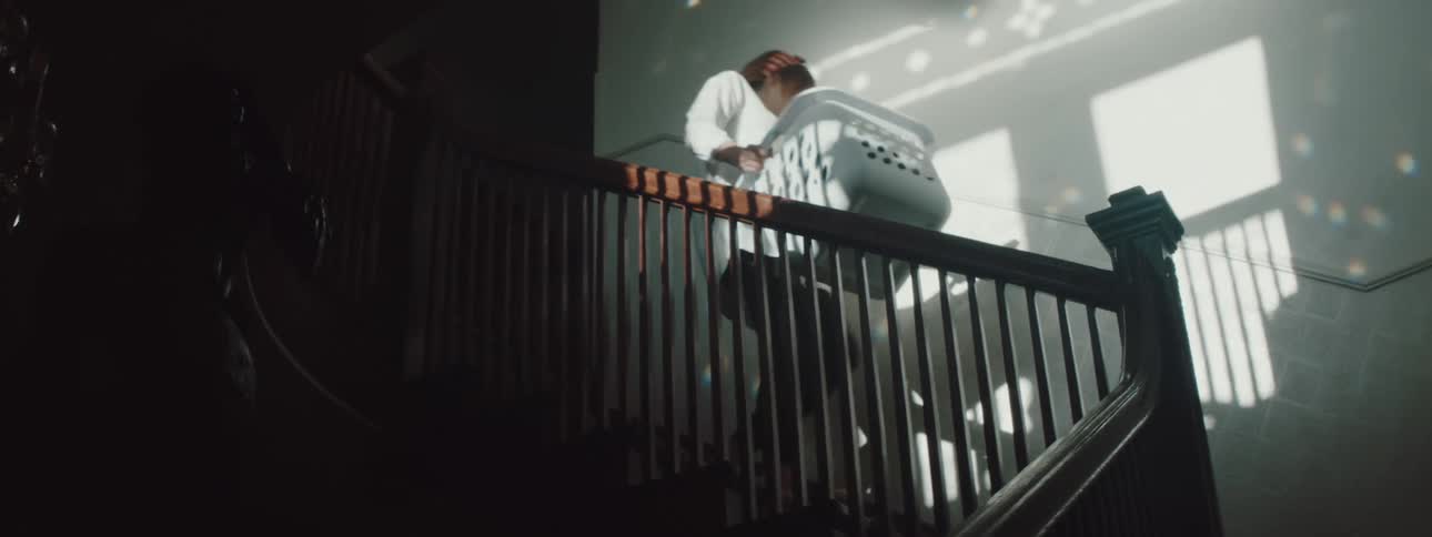 A woman walking down a staircase with a laundry basket as a man walks behind her carrying boxes