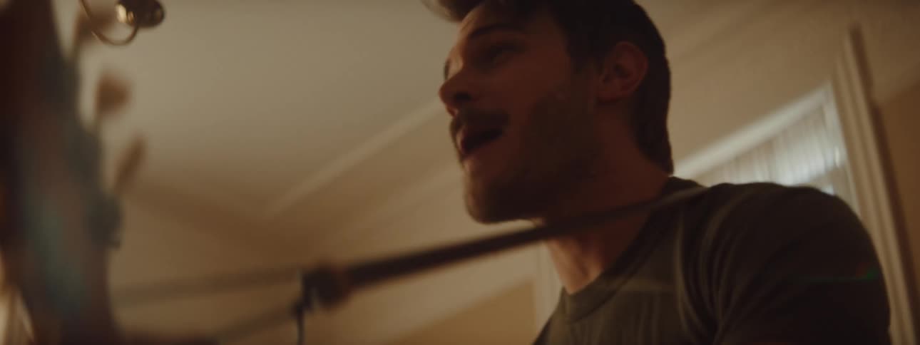 Man with a beard and a shirt plays guitar and sing song in room