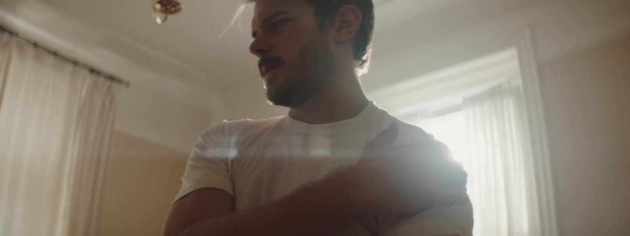 A man is stretching his arm and standing inside of his house