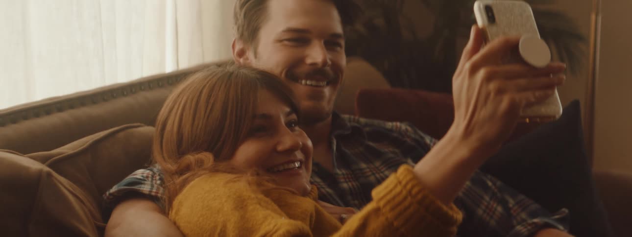 Couple cuddles lying on couch sharing use of mobile phone