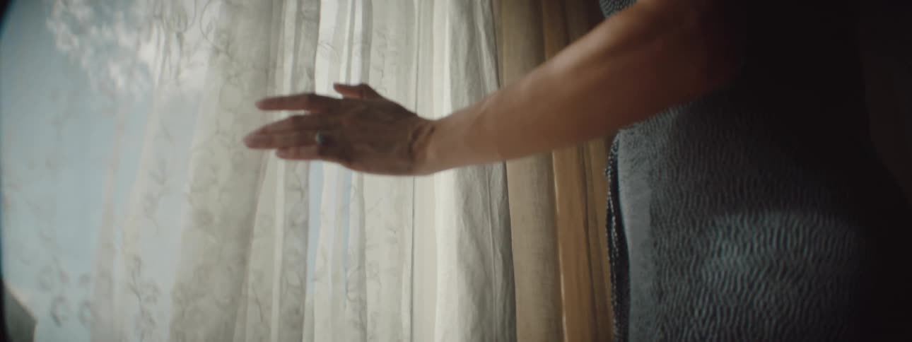 A woman is walking in her house and looking at a window
