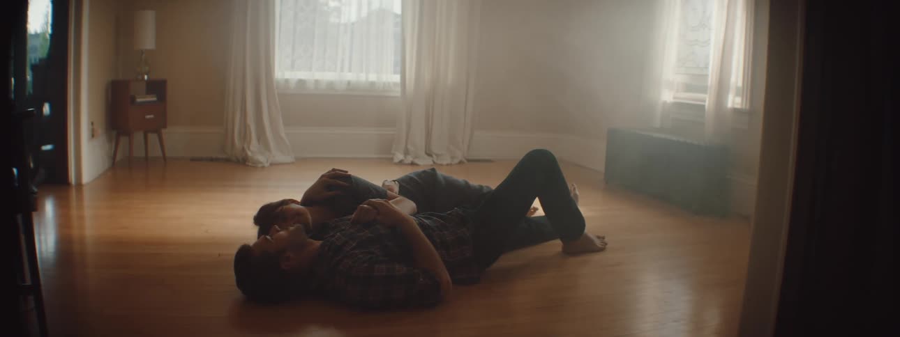 Man and woman lies down on the floor and hold each other in empty room