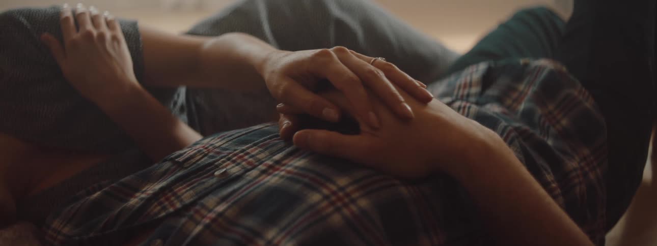A man and a woman in a room laying on the floor as she caresses his hand