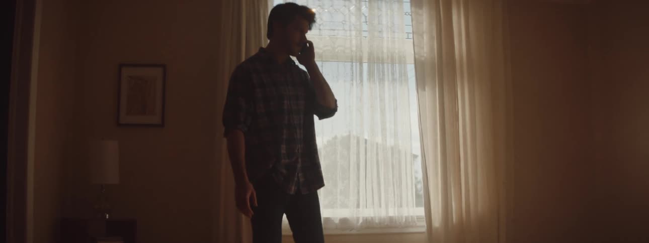 Man in silhouette against the window talking on smartphone and walking up and down the room