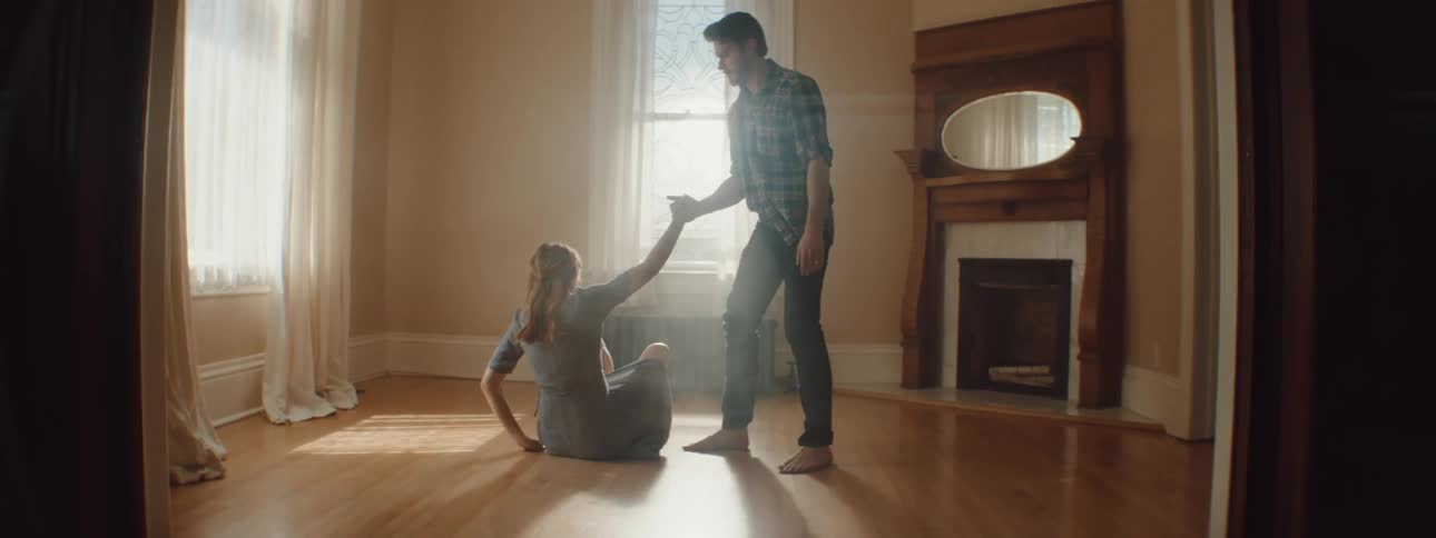 Man helps pregnant woman stand up from floor in unfurnished room