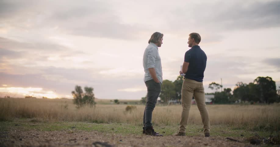 Two men gesture and talk in a wide open field