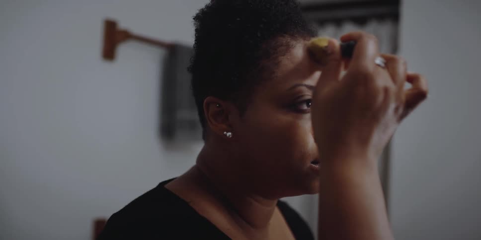 A woman looks at herself in the mirror while she applies makeup to her face with a makeup brush