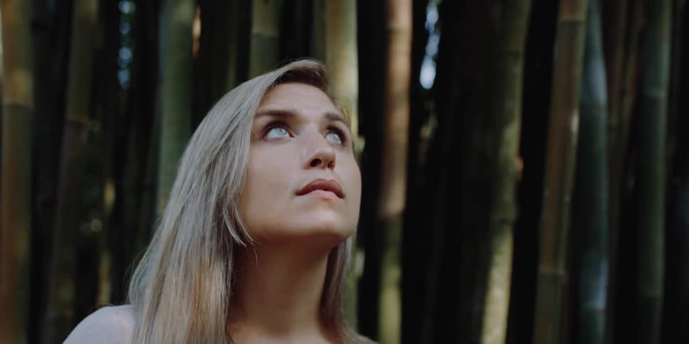 Blonde woman with hazel eyes looks up in front of trees