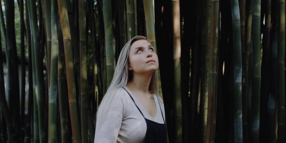 A young woman stands in a bamboo grove and looks around
