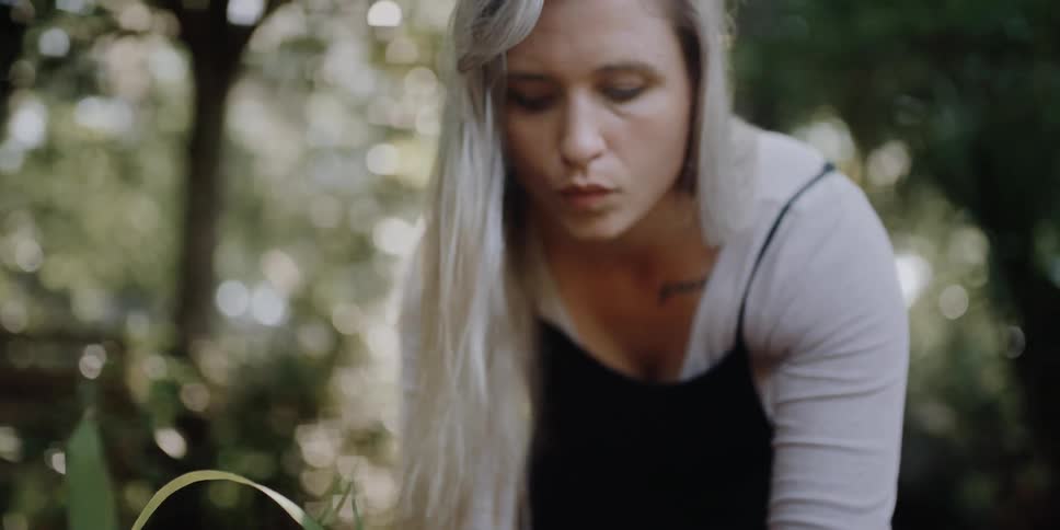 A woman with a ring in a garden touching a plant with trees in the background
