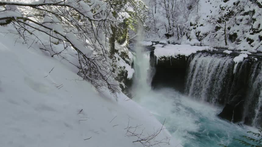 A huge amount of snow falls from a tree into a pristine waterfall in the heart of winter on the shortest day of the year near the winter equinox