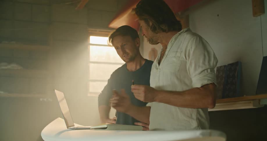 Two men go over the design of a surfboard