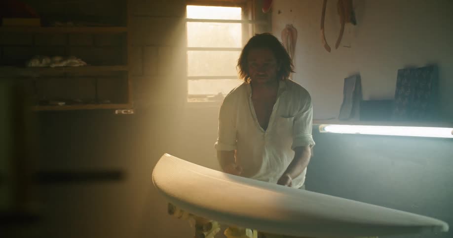 A white male in a workshop area inspecting a surfboard