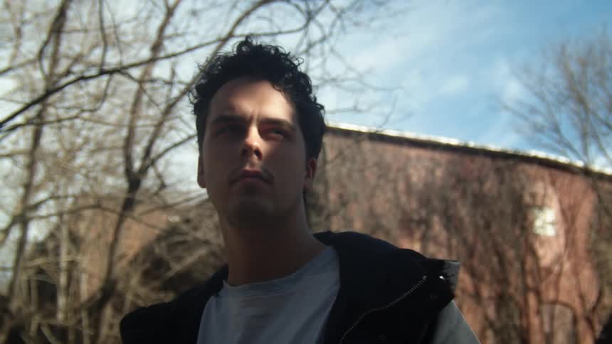 Man with a shirt and a black coat looks around in the neighborhood