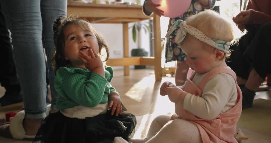 Two babies sit on the floor talking at a party