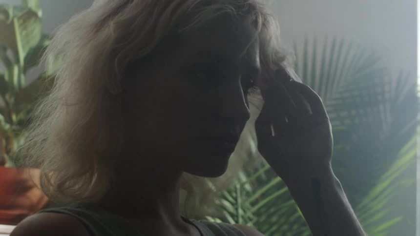 A woman standing in a room with plants a wall and a window in the background