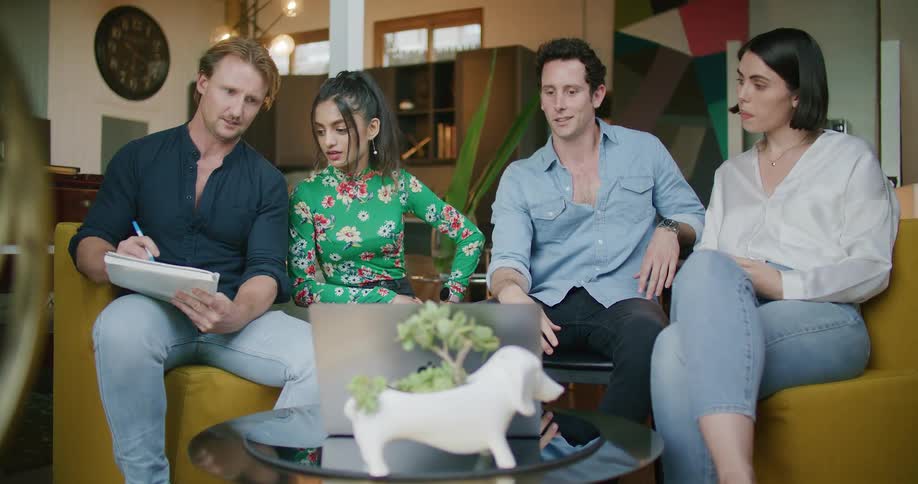Group of people sitting in the living room gathered around a laptop have an online meeting