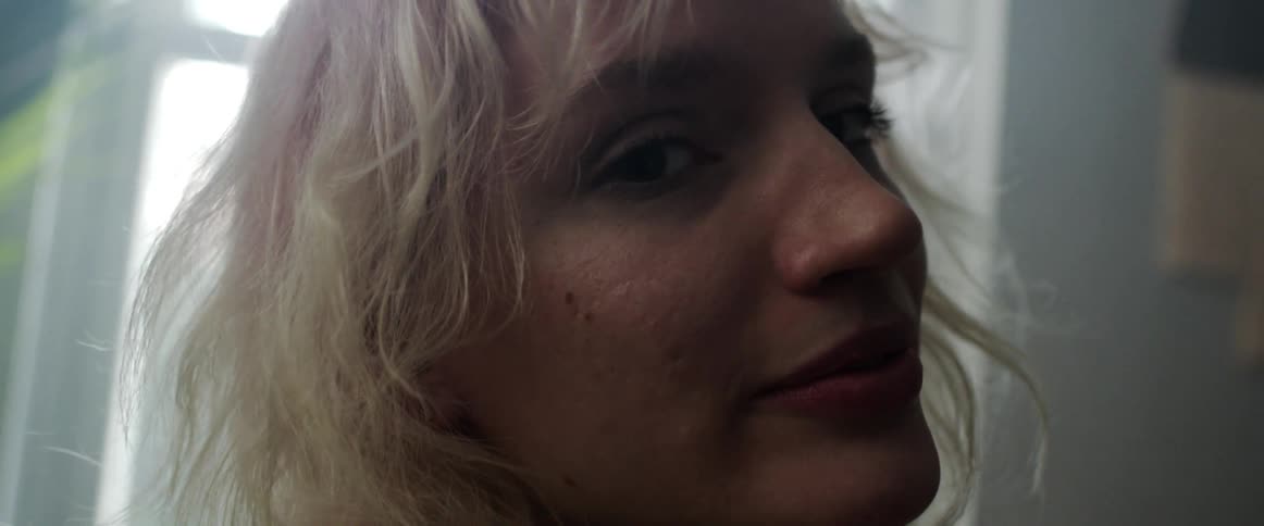 A woman in a room staring with plants a wall and a window in the background