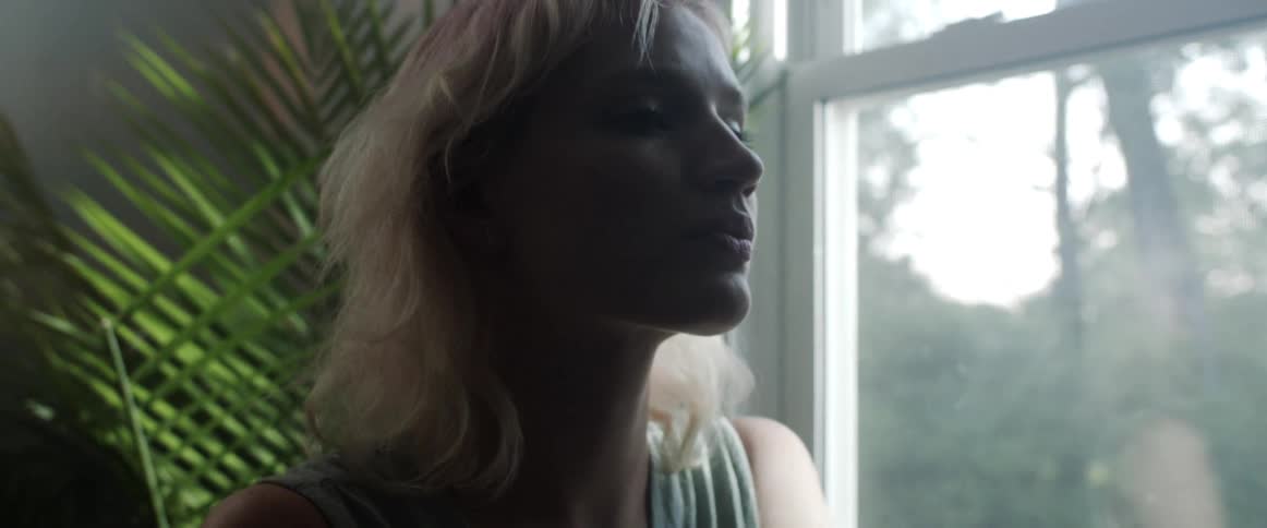 A woman is sitting indoors and looking out the window