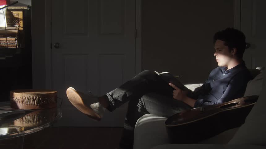 Man sitting on a couch in the dimlyh lit living room reading a book