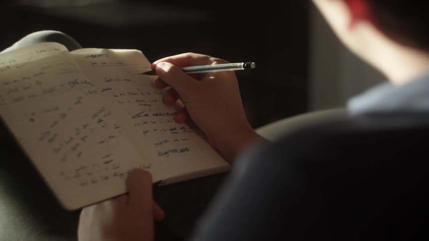 A person is sitting indoors and writing in a journal