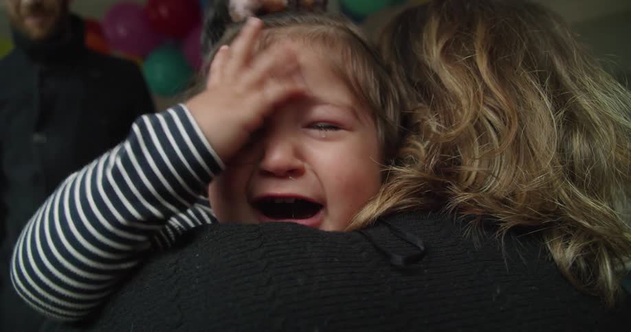 Blonde woman with a black sweater holds toddler girl crying