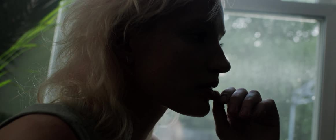Side view of blonde woman touching her lips and stands by the window is silhouetted against the light