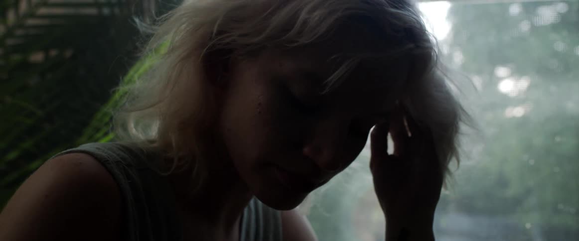 Blonde woman with a grey sleeveless shirt touching her hair is silhouetted against the window