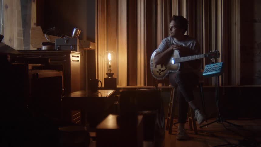 A man is sitting on a stool with a guitar