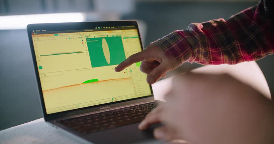 A 3D surfboard simulation is shown on a laptop screen