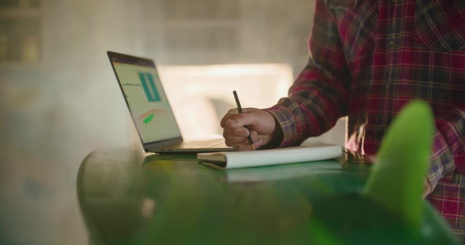 Man stands making notes based onimage on screen of laptop sitting on green surfboard shaped platform