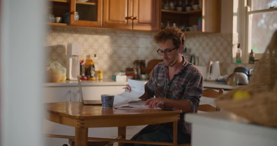 A man sits at a table at home and goes through paperwork