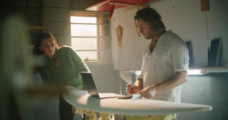 Client and customer checking a laptop placed on the surface of a surfboard in a workshop