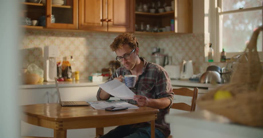 Man reading documents on the kitchen table at home while drinking a hot beverage