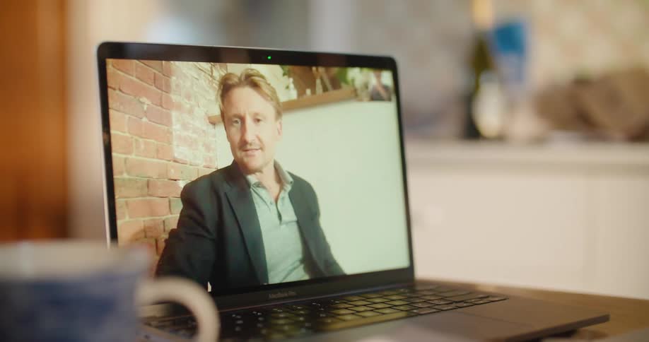 Man talking on a video call through a laptop waves his hand in a greeting