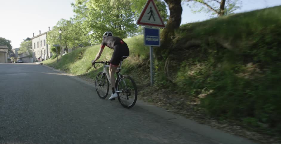 A man in black bikes down a street