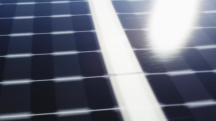 Skimming just above a row of solar panels with sunshine reflecting off the surface