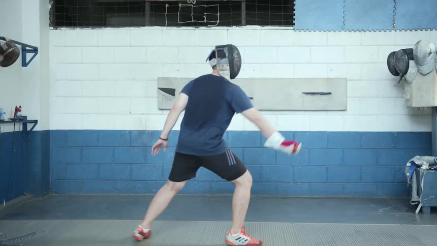 A man is practicing fencing in the gym