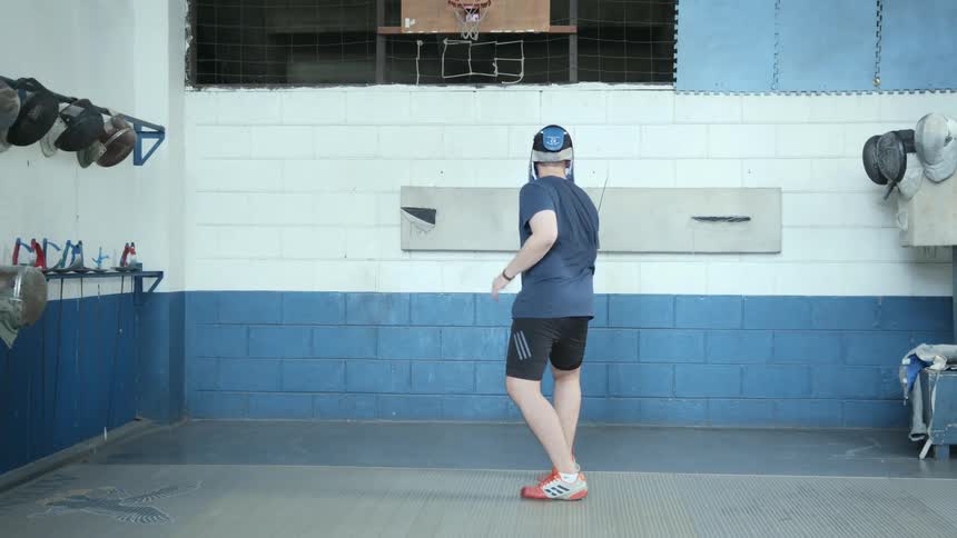 A man is practicing fencing while inside of a gym