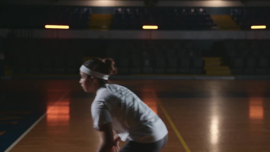 Teenage girl dribbling a basketball inside a dimly lit court