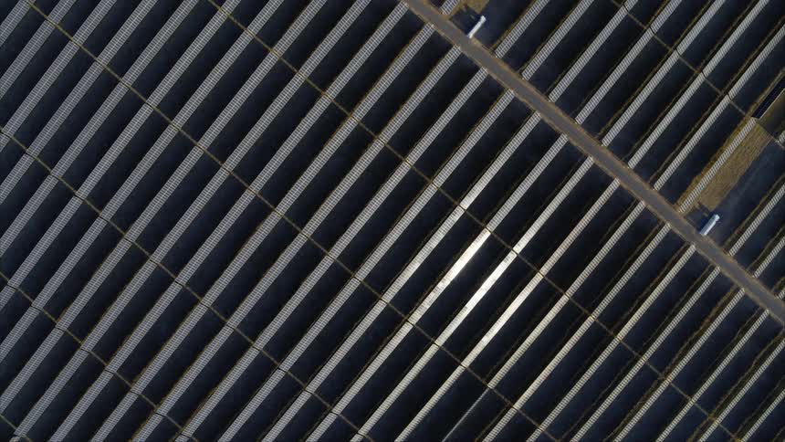 Sunlight glints off parallel rows of solar panels lined up on a large utility scale solar farm