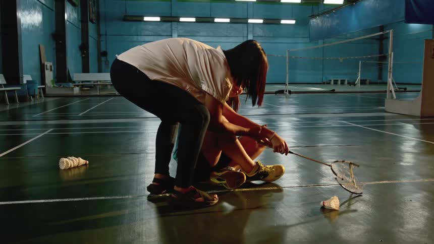 Woman sitting on the floor with a broken badminton racket gets help from a coach