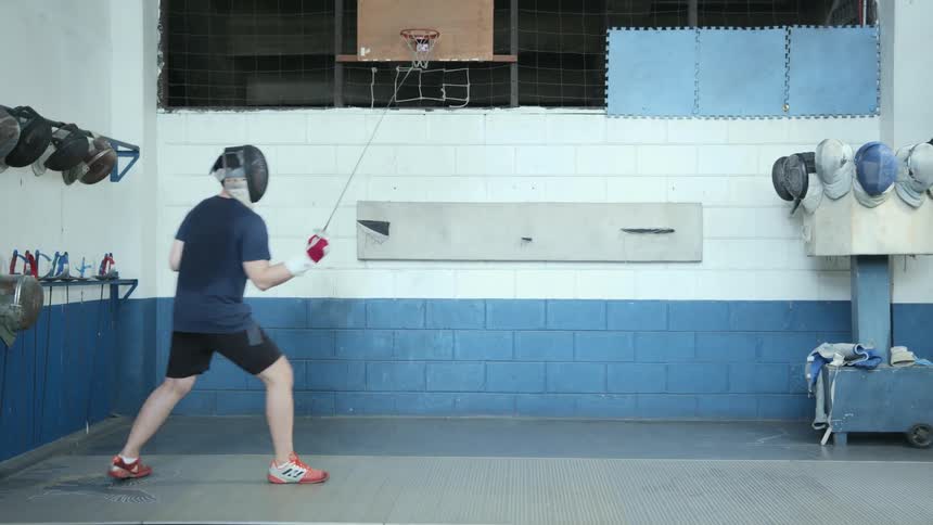 A man with a fencing mask and sword practicing in a room with a wall in the background