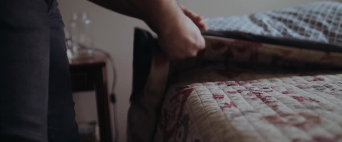 A woman smooths out wrinkles in her quilt while making her bed