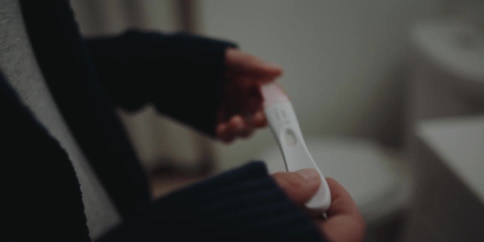 A person in a bathroom picking up a pregnancy test with a sink and toilet in the background